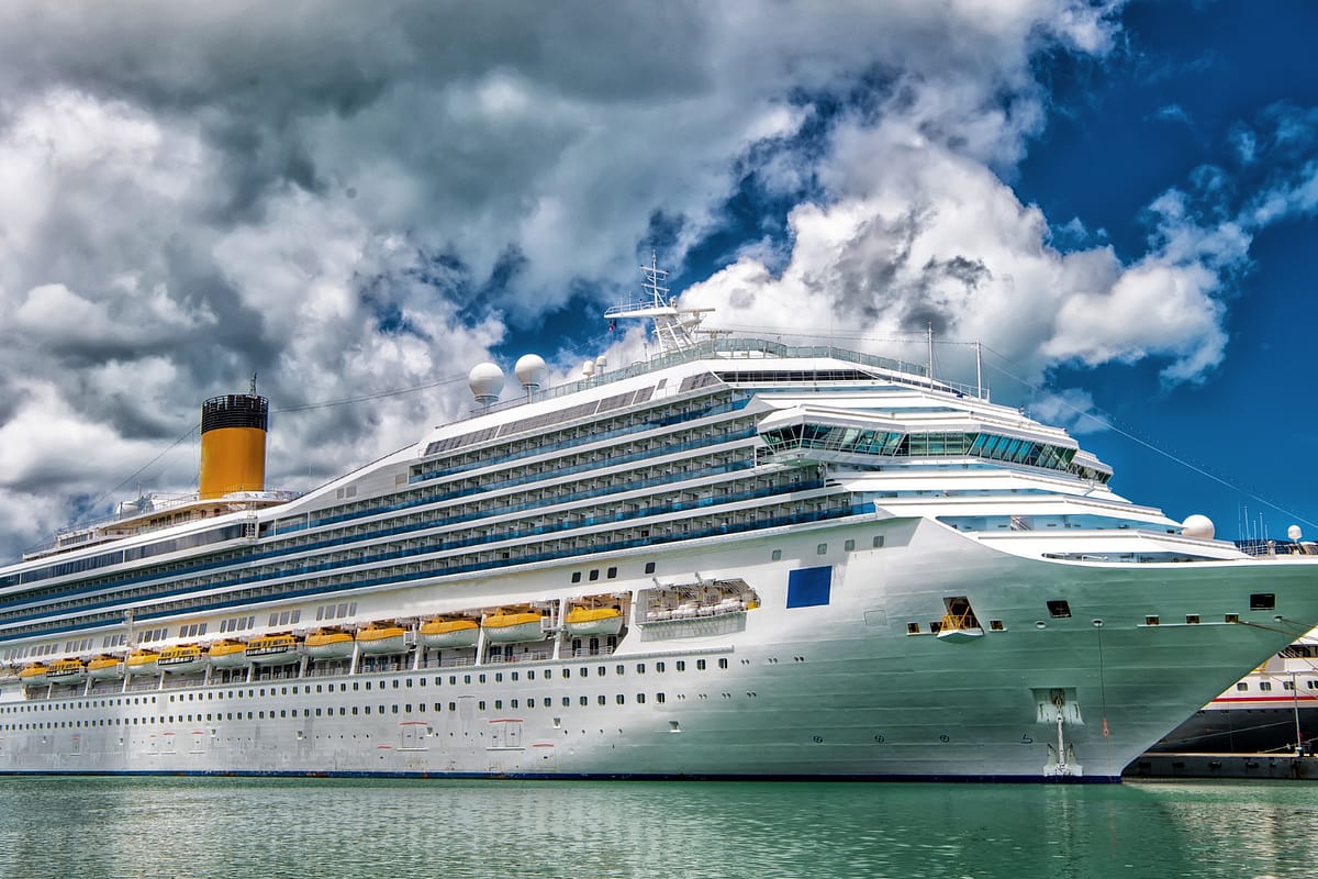 Large white cruise ship docked at port under blue sky with clouds, representing 7-day cruise cost breakdowns for 2025.